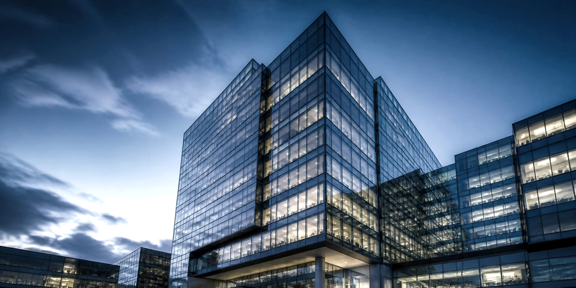 Glass and steel commercial office towers photographed from below at blue hour